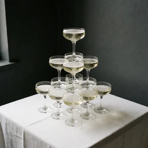 Stacked champagne flutes with foam on a white table with napkins against a black background, suitable for elegant catering events.