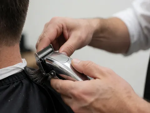 Detailed view of professional electric hair clippers resting on a clean white surface, highlighting the tool used in barbershop services for precise haircuts and beard trims.