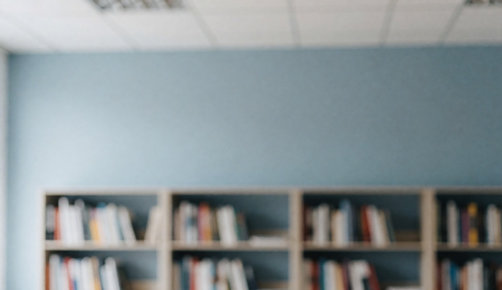 A softly blurred office interior featuring a bookshelf filled with books against a blue wall, serving as a professional background for text.