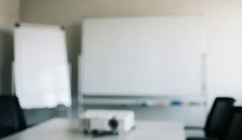 Empty conference room featuring a whiteboard, projector, office chairs, and a large table, providing a professional background for text.