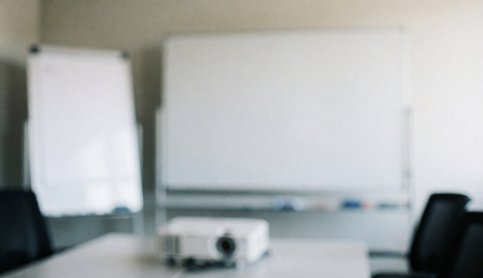 Empty conference room featuring a whiteboard, projector, office chairs, and a large table, providing a professional background for text.