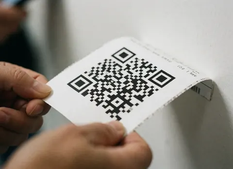 Close-up of hands holding a travel ticket featuring a QR code against a white background, highlighting details for travel agency use.