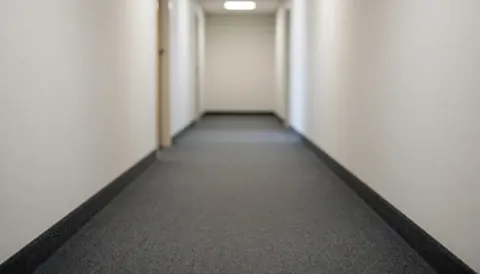 A blurred image of a residential hallway with carpeted floor and walls, serving as a clean background for text overlays.