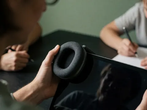 Close-up view of headphones and a tablet on a desk with learning tools, set against a soft green background for a professional studio atmosphere.