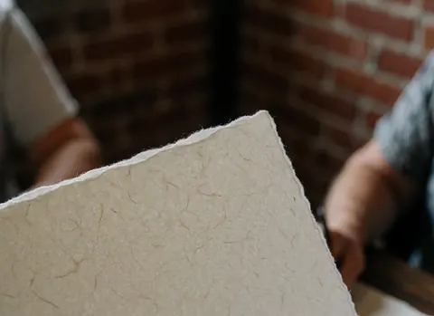 Hands holding high-quality paper with visible texture and torn edges against a red brick wall background for bookstore use