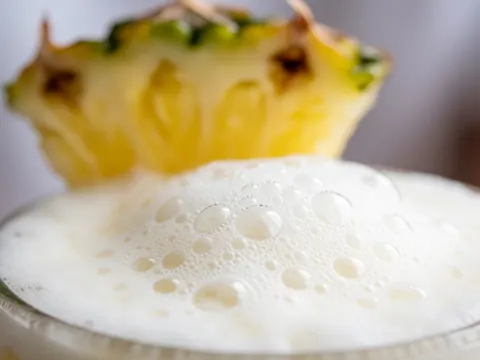 Glass of pina colada with white foam and bubbles, pineapple in the blurred background, ideal for bar and cocktail use