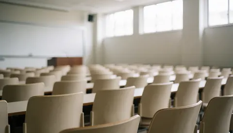 Empty university classroom featuring rows of beige chairs, a whiteboard, and a podium, illuminated by natural light from windows, suitable for text backgrounds.