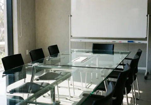 Empty modern conference room featuring a glass table, black chairs, and a whiteboard on a concrete wall, ideal for business meetings and productive work.
