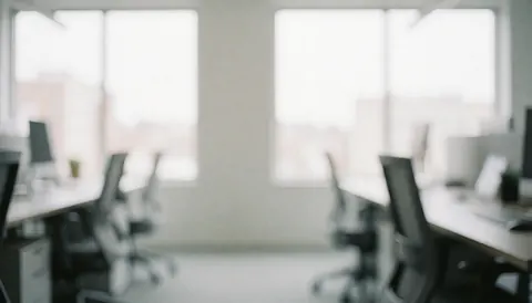 A bright and airy modern office desk with a chair near a window, featuring natural light and a blurred professional background suitable for text overlay.