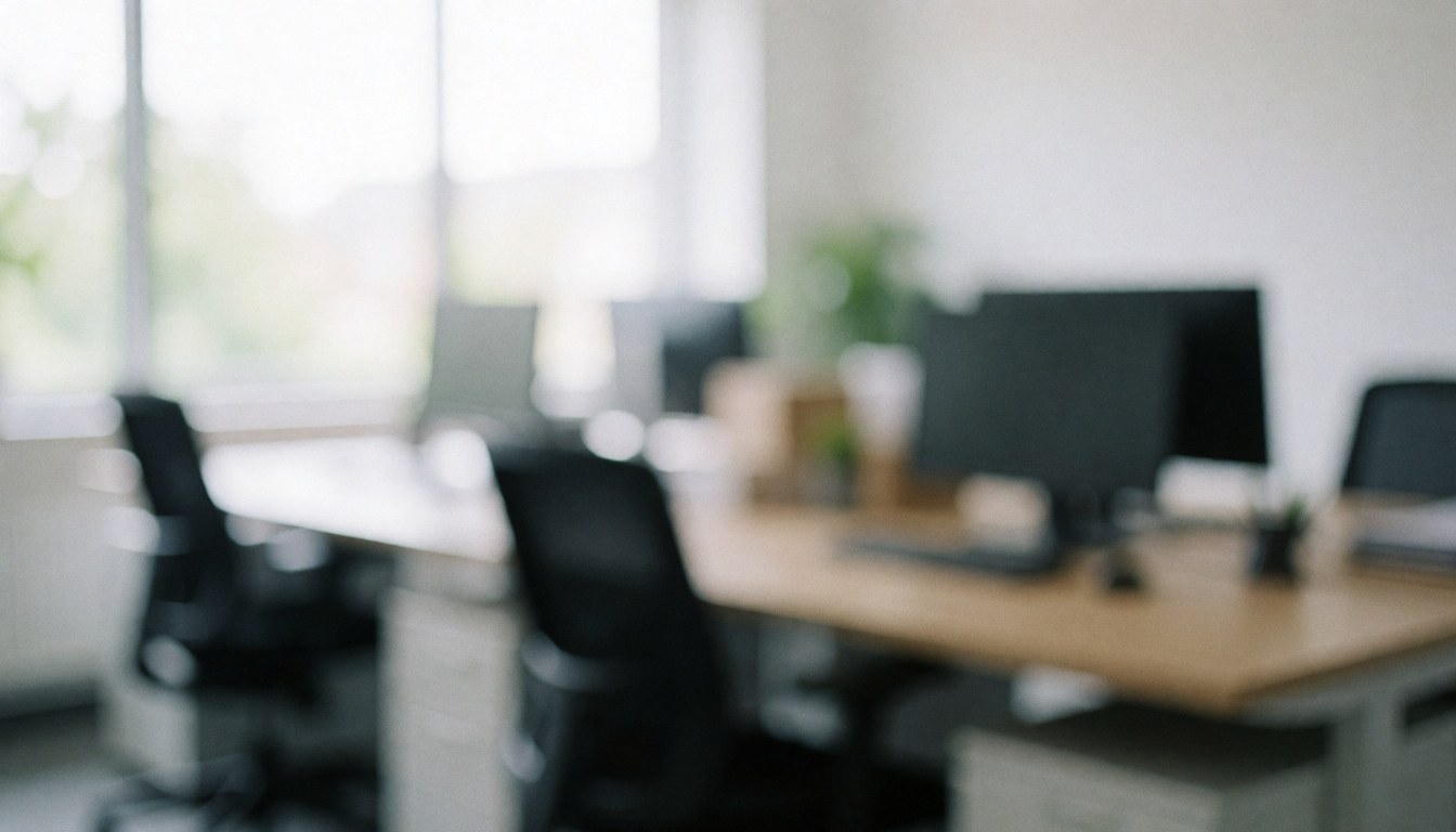 Soft focus view of a modern office with desks, chairs, and computers, illuminated by natural window light, creating a calm professional atmosphere for text overlay.