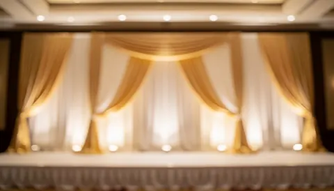 Event stage featuring golden and white curtains with warm lighting, providing a soft background suitable for promotional text and catering presentations.