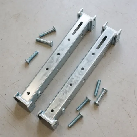Two galvanized steel air conditioning mounting brackets with loose screws on a concrete floor, diffused lighting for technical catalog use
