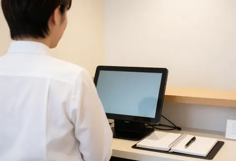 Receptionist at a barbershop looking at the POS screen with a notebook and pen on the desk against warm walls in a professional setting