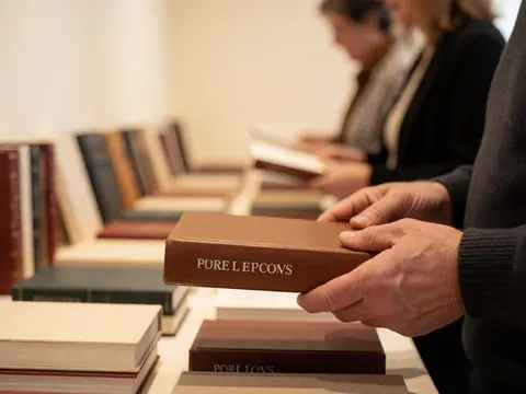 Close-up of hands holding a hardcover book with an embossed title, with other books visible in the blurred background of a bookstore.