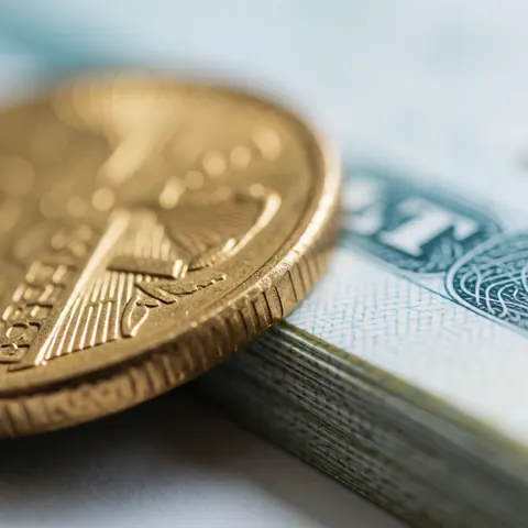 A detailed macro view of tangible financial assets including gold coins, paper certificates, and bonds arranged on a light background with soft lighting and blue accents.