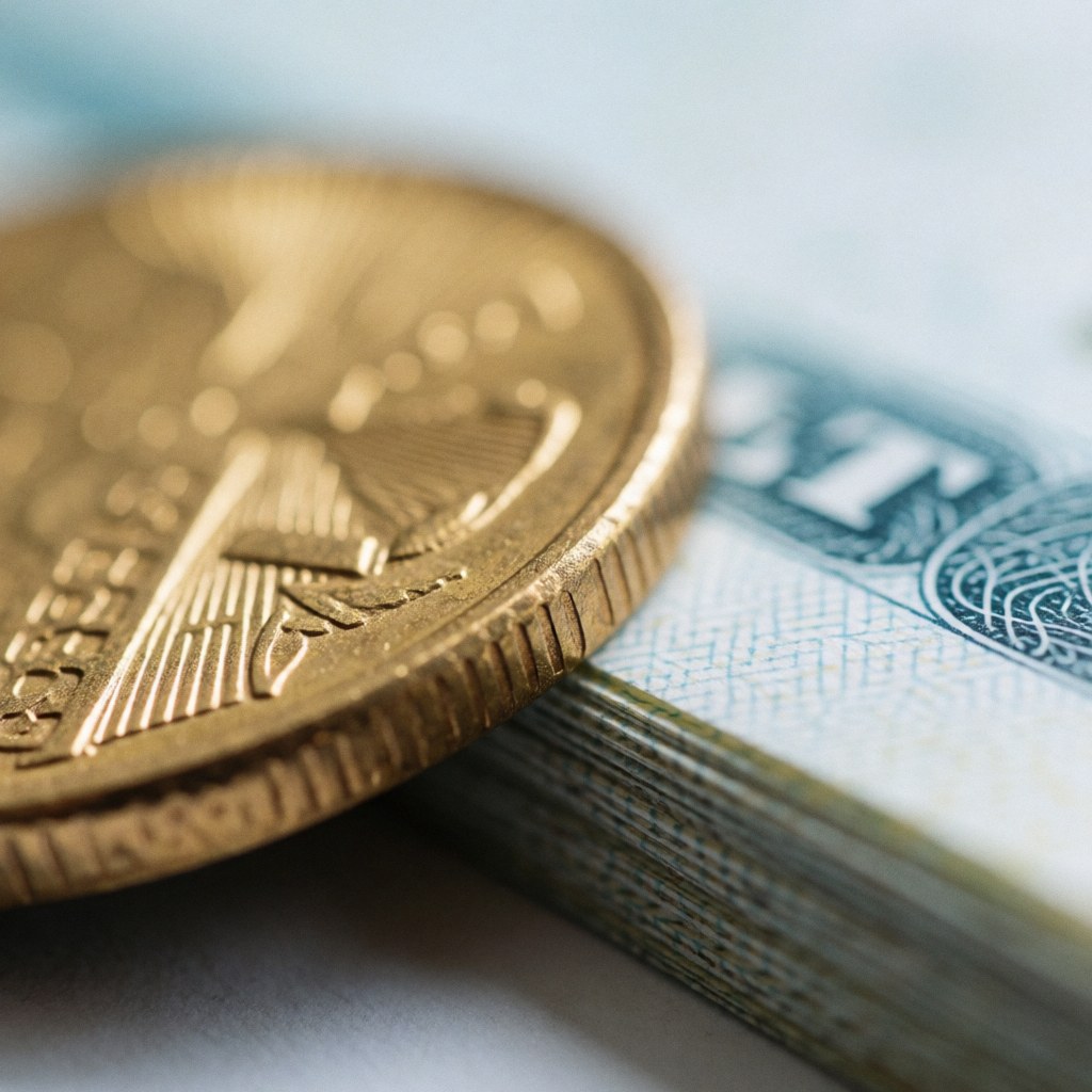A detailed macro view of tangible financial assets including gold coins, paper certificates, and bonds arranged on a light background with soft lighting and blue accents.