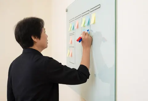 Manager writing on a whiteboard with colorful post-its, planning a sprint in a modern office with professional lighting and organized workspace.