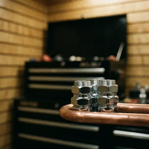 Shiny chrome pipe connectors and copper tubing arranged on a workbench with blurred background