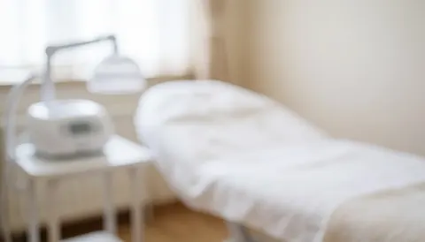 Soft beige background of an aesthetic clinic featuring a treatment bed and medical equipment, ideal for professional text overlays and presentations.