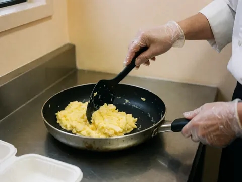 Close-up view of scrambled eggs being stirred in a stainless steel nonstick pan with a spatula, highlighting a clean and hygienic fast food preparation process.