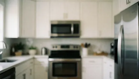 Blurred background of a modern kitchen featuring white cabinets and stainless steel appliances, suitable for text overlay in real estate marketing materials.