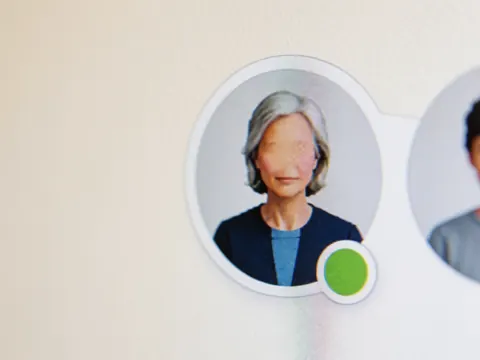 Close-up of a digital user avatar icon displaying a green status indicator on a screen against a warm-colored wall background