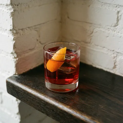 A classic Negroni cocktail served in a short glass with ice and an orange slice on a dark wooden bar with a brick wall background