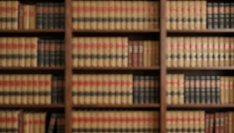 A stack of leather-bound law books resting on a wooden shelf, creating a professional background with soft bokeh for text overlay