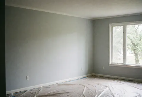 Interior of a gray painted room with natural light coming through a window and floor covered in protective plastic for construction or renovation work