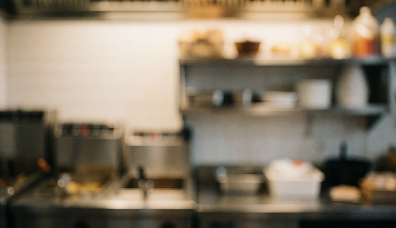 Blurred fast food kitchen background featuring fryers and shelves with warm lighting, ideal for text overlay in a professional setting