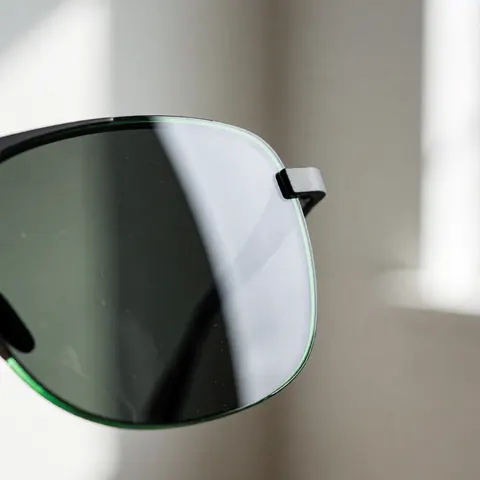 Detailed close-up view of a hydrophobic optical lens surface featuring distinct water droplets beading up, highlighting the water-repellent coating technology used in high-quality eyewear.