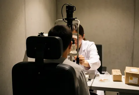An optometrist performs a professional eye exam on a patient seated in a chair using specialized optical equipment in a clinical setting