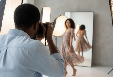 A fashion model stands in a bright photo studio with professional lighting and a mirror, capturing a dynamic portrait for business use.