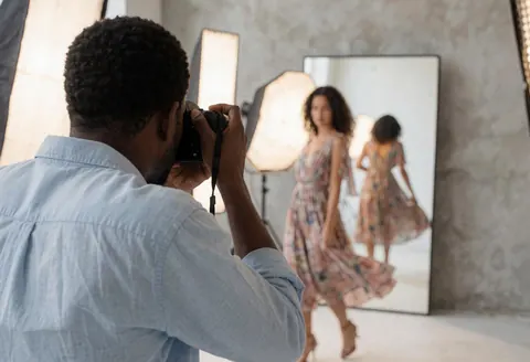 A fashion model stands in a bright photo studio with professional lighting and a mirror, capturing a dynamic portrait for business use.