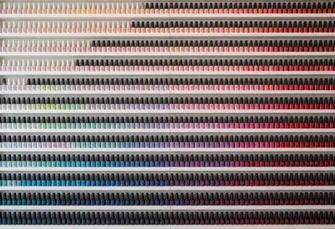 Shelves filled with hundreds of nail polish bottles arranged in a gradient from pastel to red colors, perfect for a professional nail salon interior.