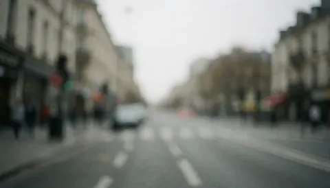 Out of focus gray urban street scene with blurred buildings and pavement under diffused light, serving as a neutral professional background for text or graphics.