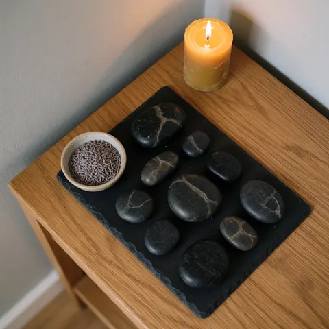 A set of smooth, heated volcanic basalt stones arranged on a wooden table, prepared for a relaxing spa treatment or therapeutic massage session.