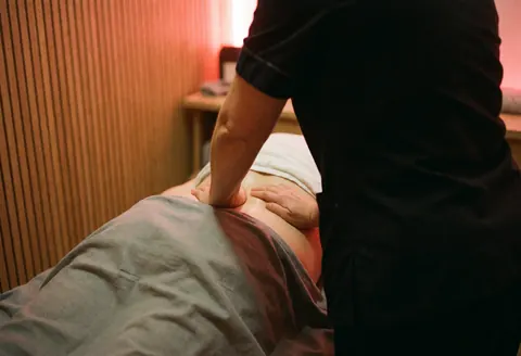 Professional therapist using firm hands to perform a therapeutic back massage on a client in a warm wooden room.