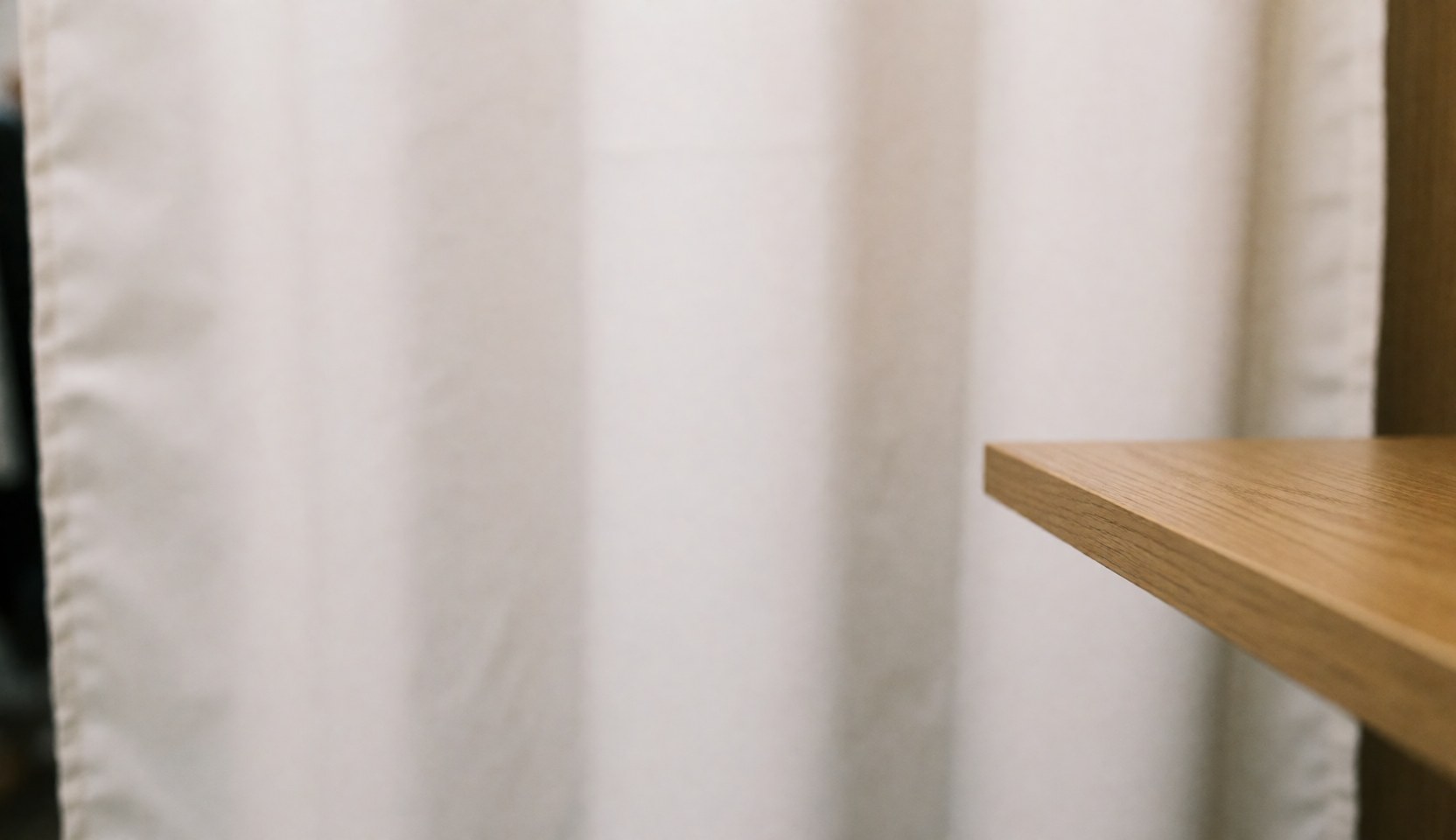 A soft white fabric curtain hanging beside a wooden shelf, creating a calm and neutral background suitable for therapeutic massage and wellness business designs.