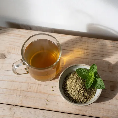 Steaming cup of yerba mate with fresh mint leaves and dried herbs on a light wooden table in natural morning light