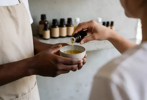 Close-up of hands preparing essential oils in a ceramic bowl for therapeutic massage service