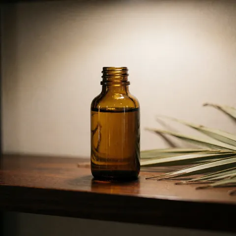 Close-up of an amber glass bottle filled with palm oil resting on a dark polished wooden shelf in a spa setting
