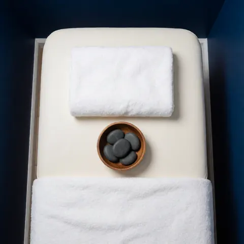 Wooden bowl holding hot basalt stones next to a white towel on a massage table for physical therapy and relaxation treatment
