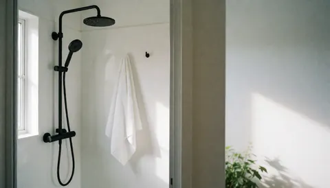 Modern design shower featuring a white towel, white walls, natural light, and a plant, suitable for spa or therapeutic massage settings.