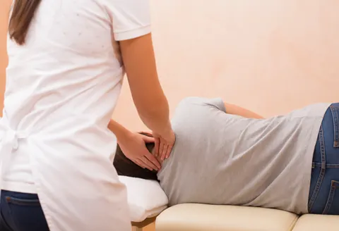 A therapist applies pressure to a client's neck during a chiropractic session in a warmly lit room with terracotta walls.