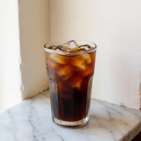A refreshing glass of iced coffee with ice cubes placed on a smooth marble surface, ideal for coffee shop product displays
