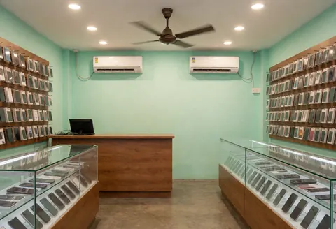 Clean and organized mobile phone shop interior featuring green walls, glass display counters, and packaged phones ready for sale.