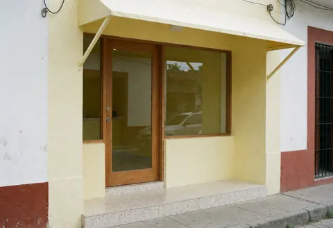 The exterior entrance of a small accounting office featuring a wooden door, yellow walls, and a tiled step leading to the street.