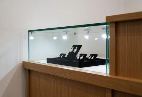 Silver earrings arranged in a glass display case on a wooden counter, illuminated by spotlights in a clean jewelry store interior
