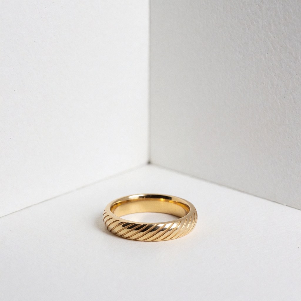 A detailed close-up of a personalized engraved gold ring displayed against a clean white background, highlighting the metal texture and craftsmanship.
